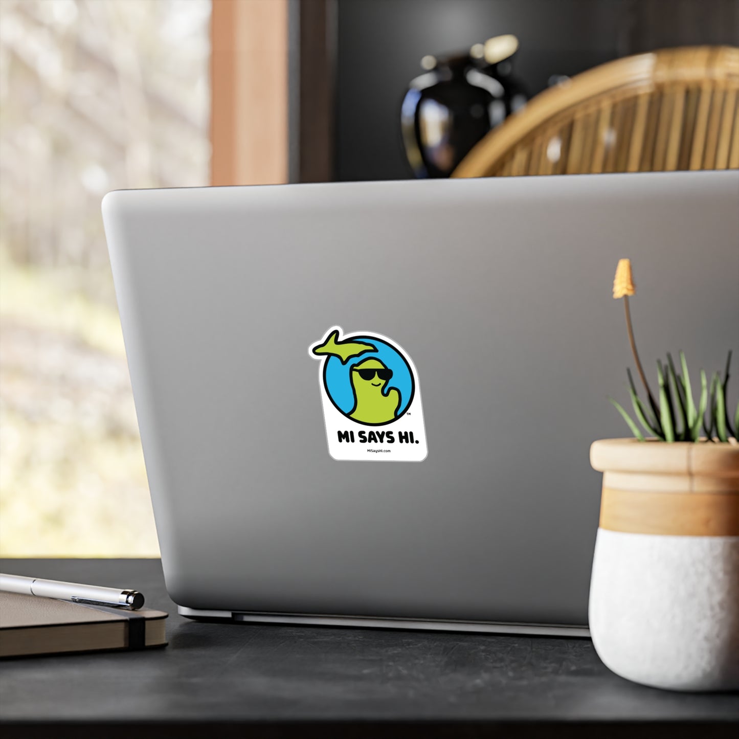 Waving Michigan logo wearing sunglasses on a vinyl sticker applied to a laptop.