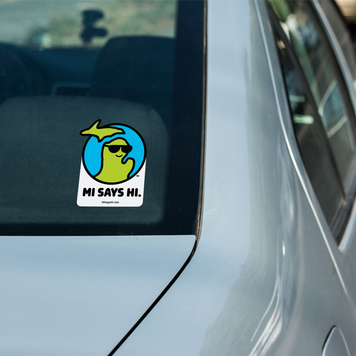 Waving Michigan sticker from the MI Says Hi™ brand on the back window of a car.