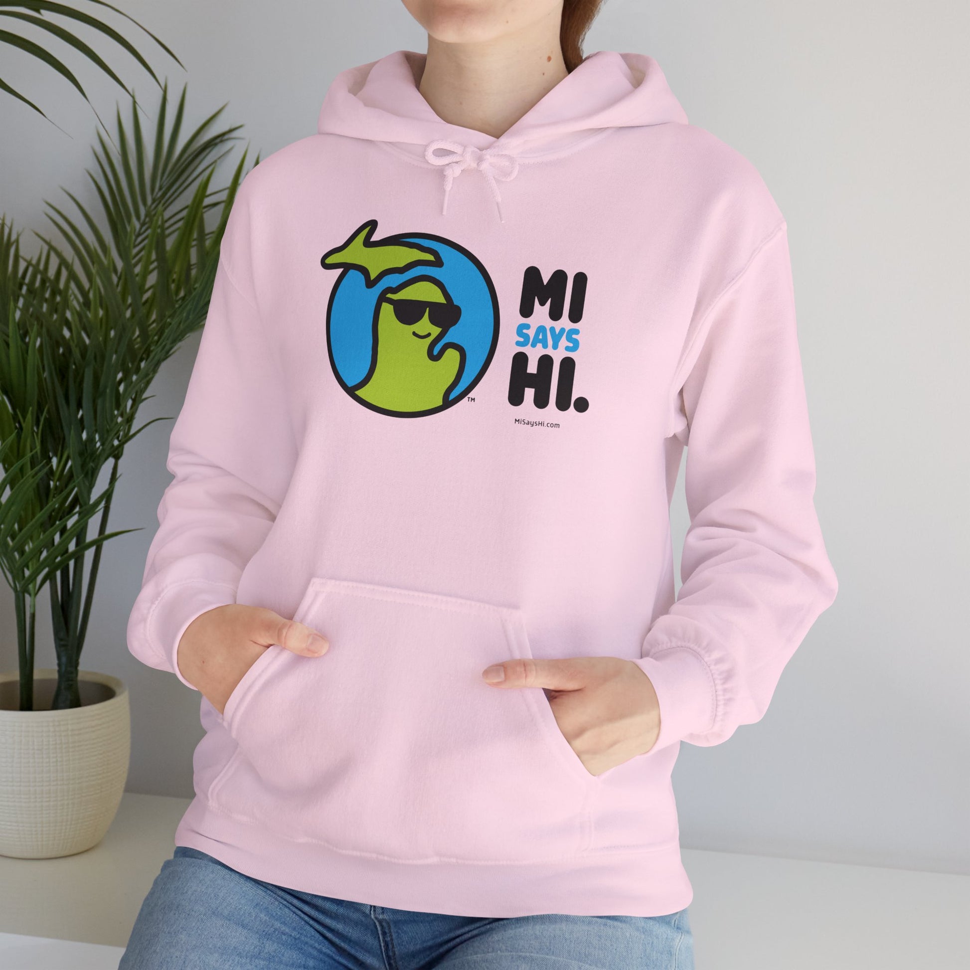 Woman wearing a pink hoodie with waving Michigan logo wearing sunglasses and smiling for the MI Says Hi brand.